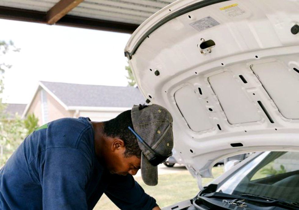 Savannah mechanic leaning into an engine bay at a carport
